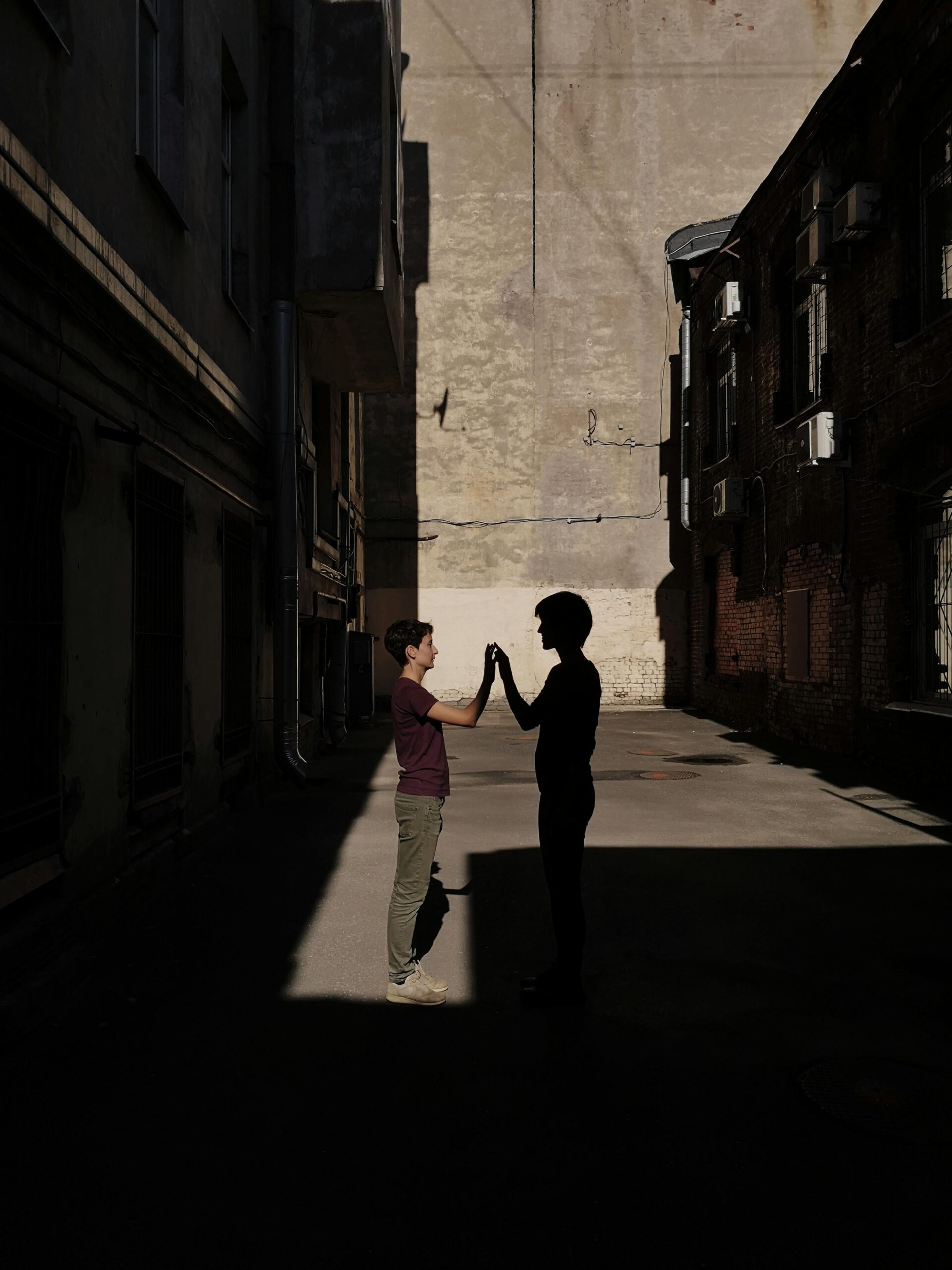 Silhouetted couple holds hands in an urban alley, creating a dramatic play of light and shadow.